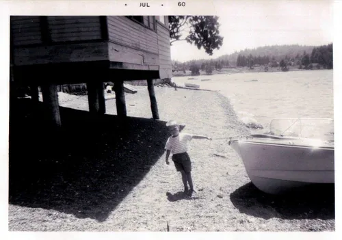 A boy at the water's edge beside the original boat house, photographed in 1960
