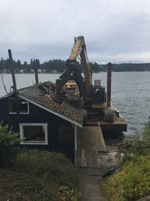 The original boat house being taken down by an excavator at the water's edge